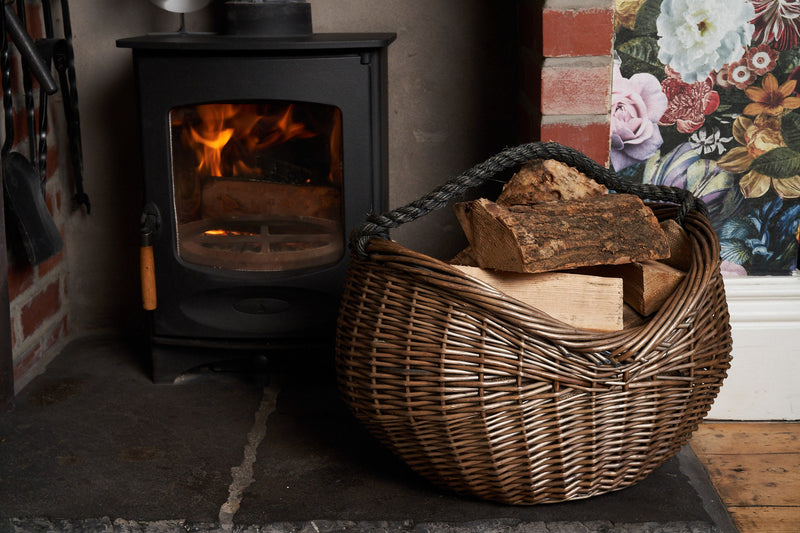 Antique Wash Large Log Basket With Black Rope Handle filled with logs in front of a fire