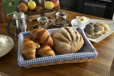Sustainable willow tray basket with gingham lining holding an array of pastries and bread